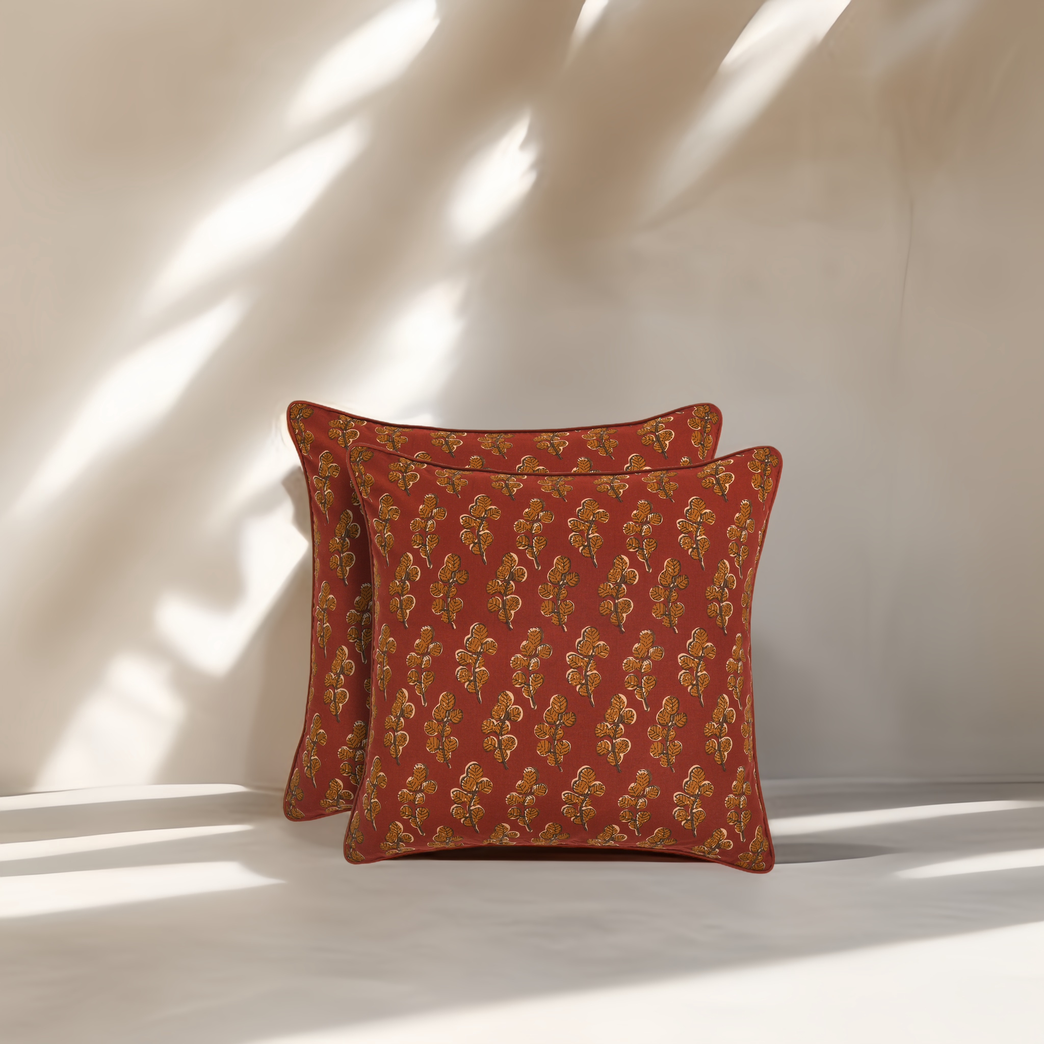 Two red patterned pillows on a white surface with soft shadows.