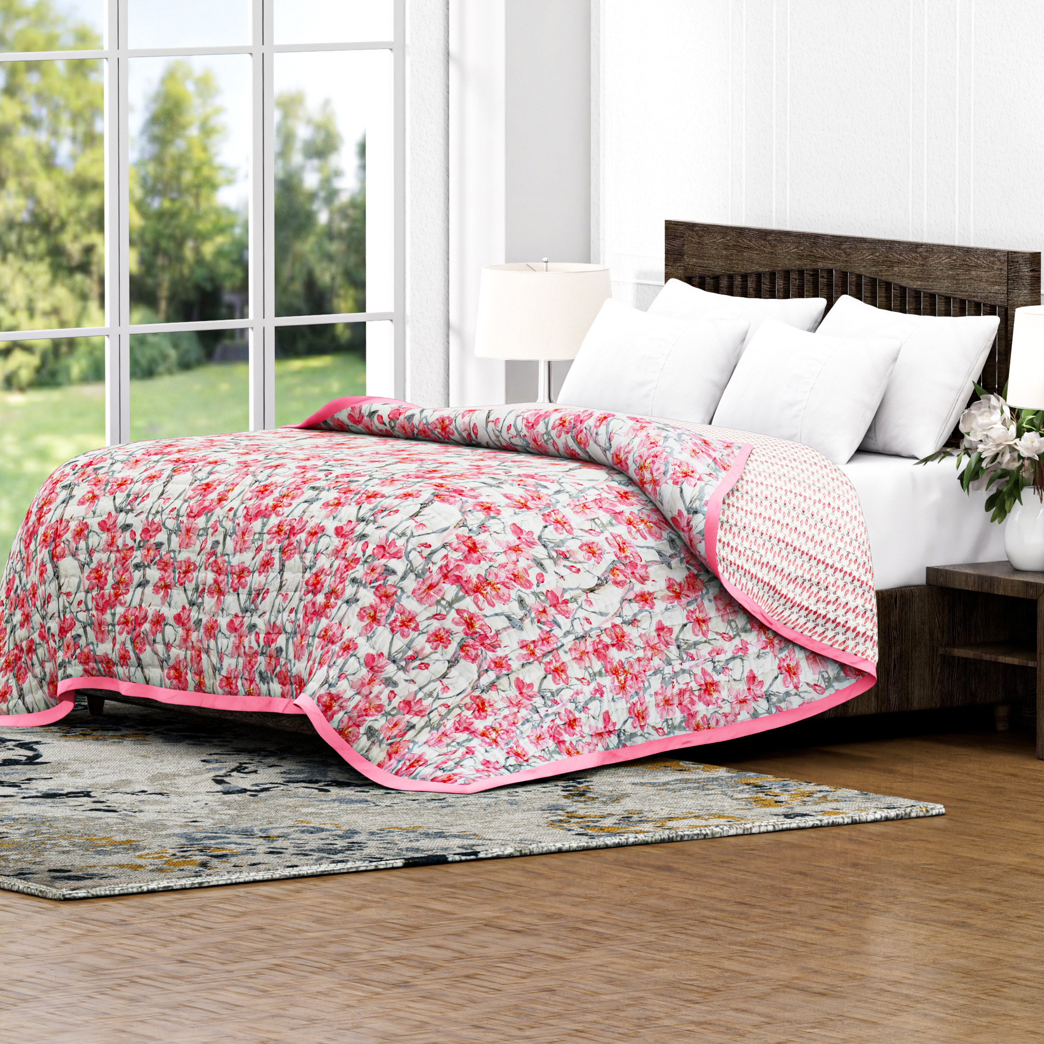 Floral quilt with pink trim on a bed in a bright room with large windows.