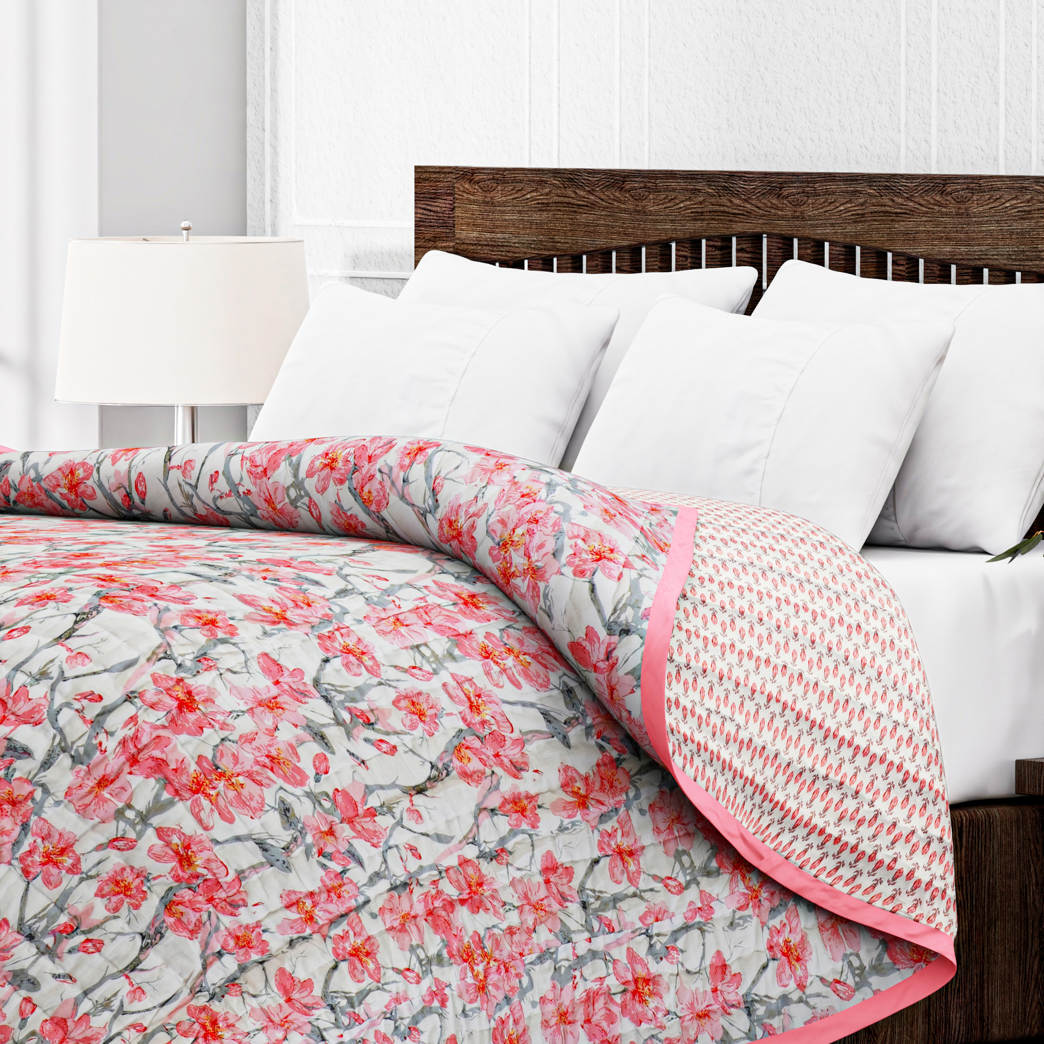 Floral quilt with pink and gray pattern on a bed with white pillows and wooden headboard.