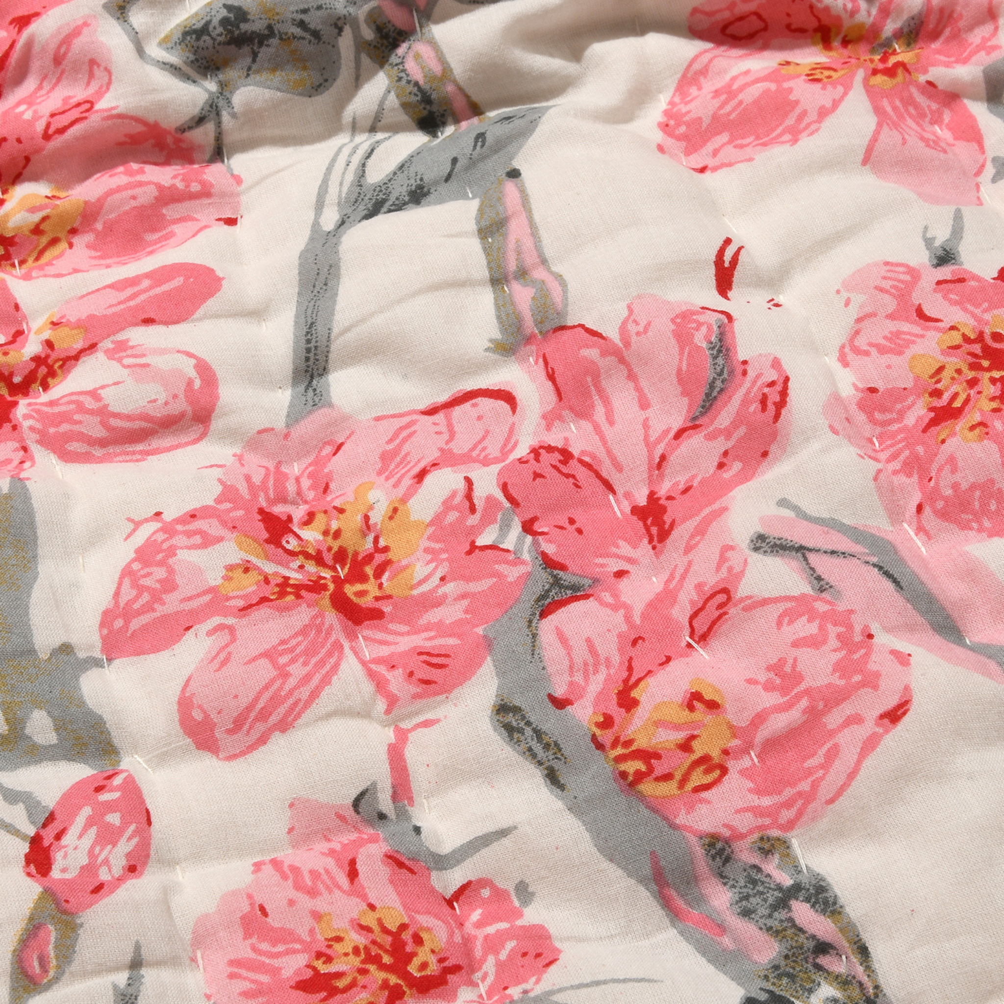 Close-up of a floral quilt with pink flowers and gray leaves on a white background