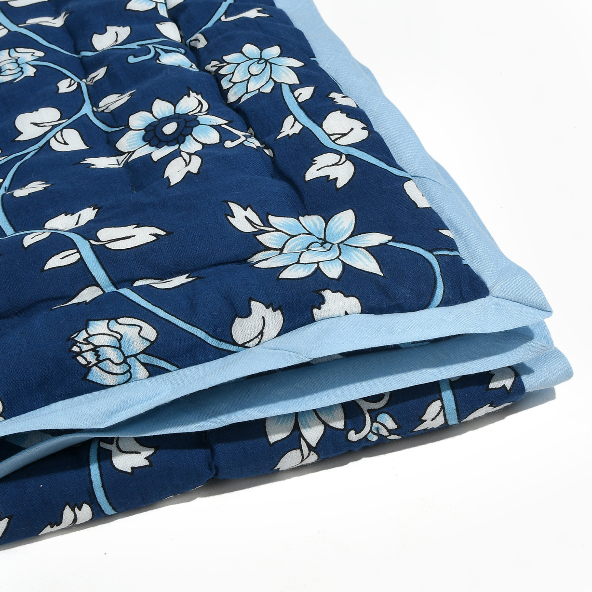 Folded blue floral quilt with white flowers on a white background