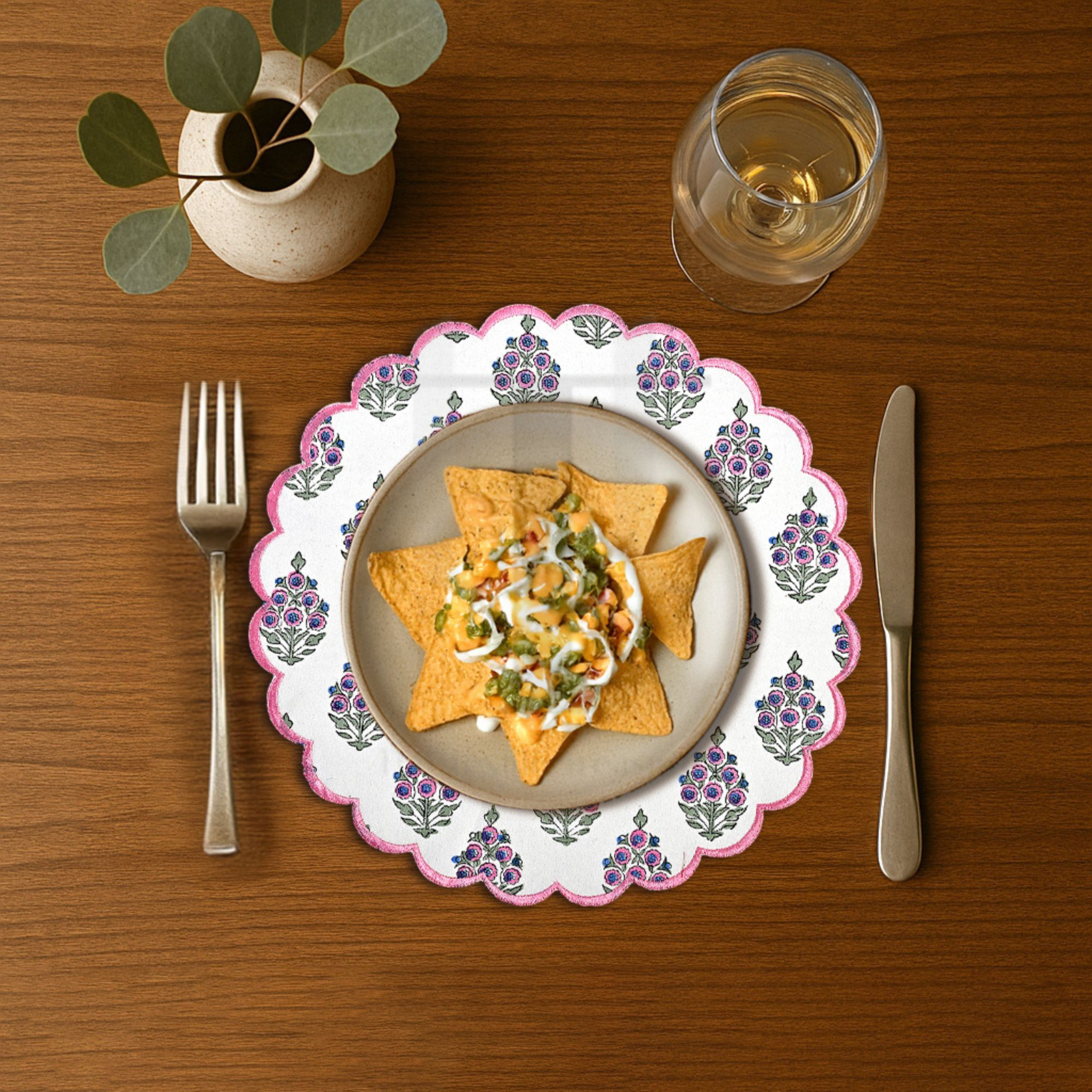 Dinner setting with a plate of nachos, a glass of water, fork, and knife on a wooden table.