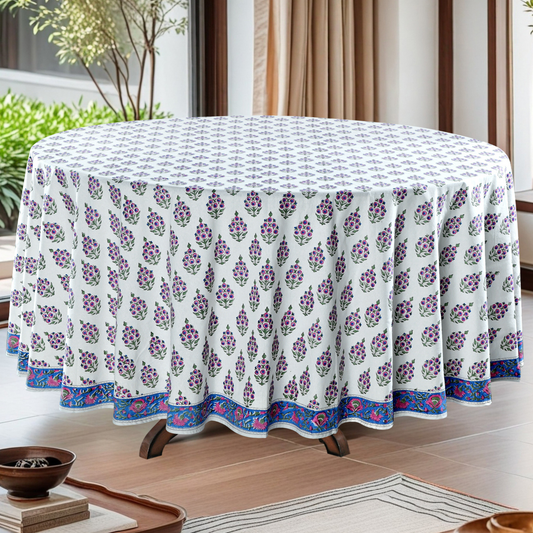 Round table with a floral patterned tablecloth in a room with plants and curtains.