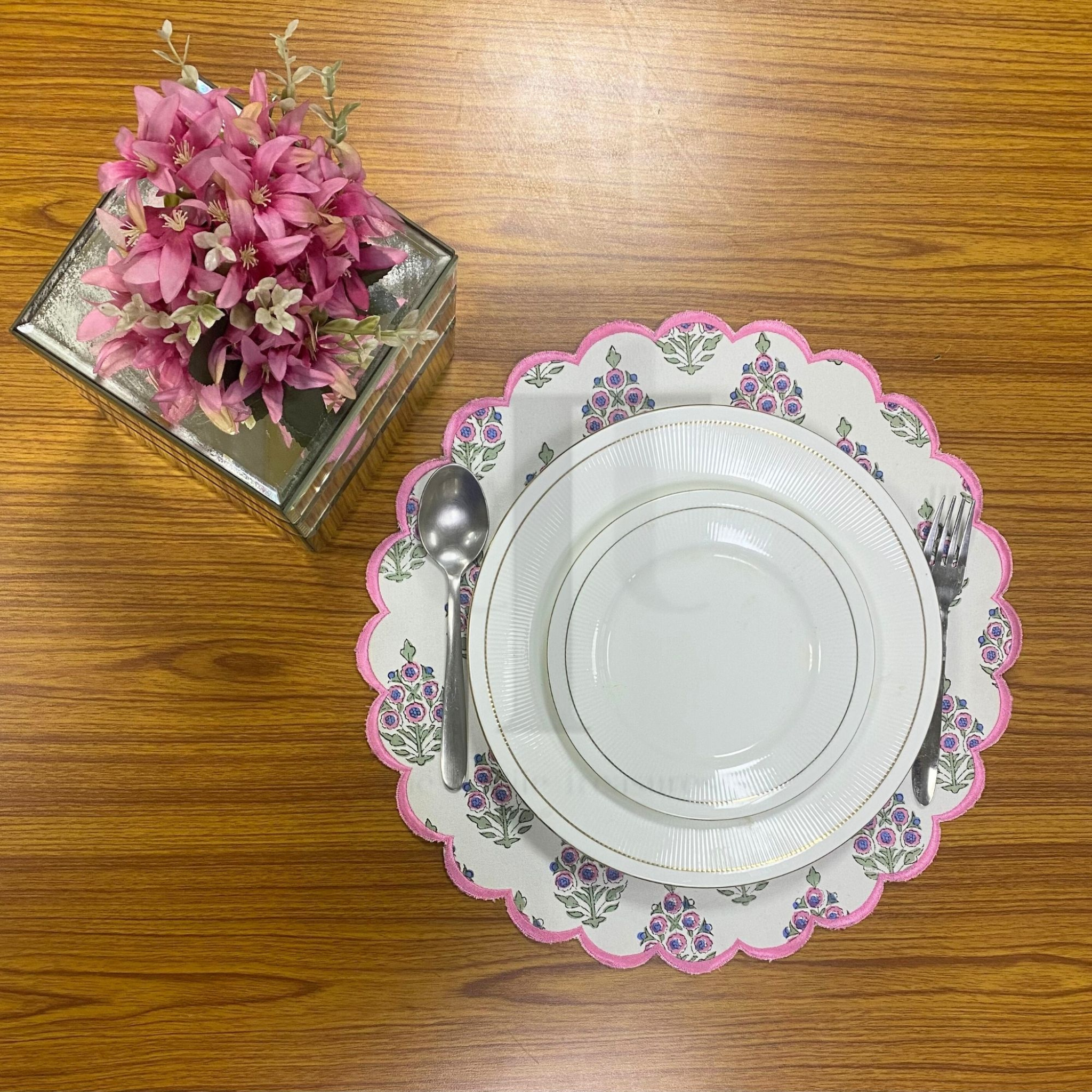Set of white plates with decorative pink rims on a wooden table, accompanied by a silver spoon and fork.