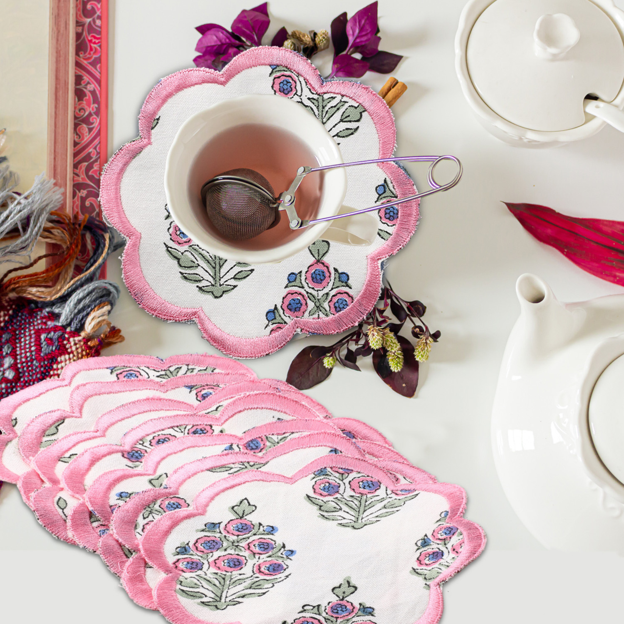 Set of pink floral coasters with a cup of tea and teapot on a table.