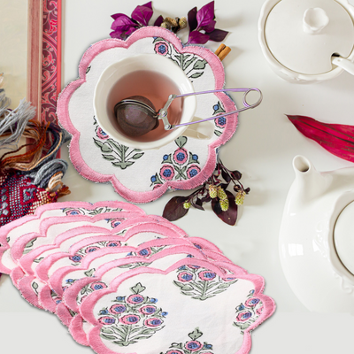 Set of pink floral coasters with a cup of tea and teapot on a table.