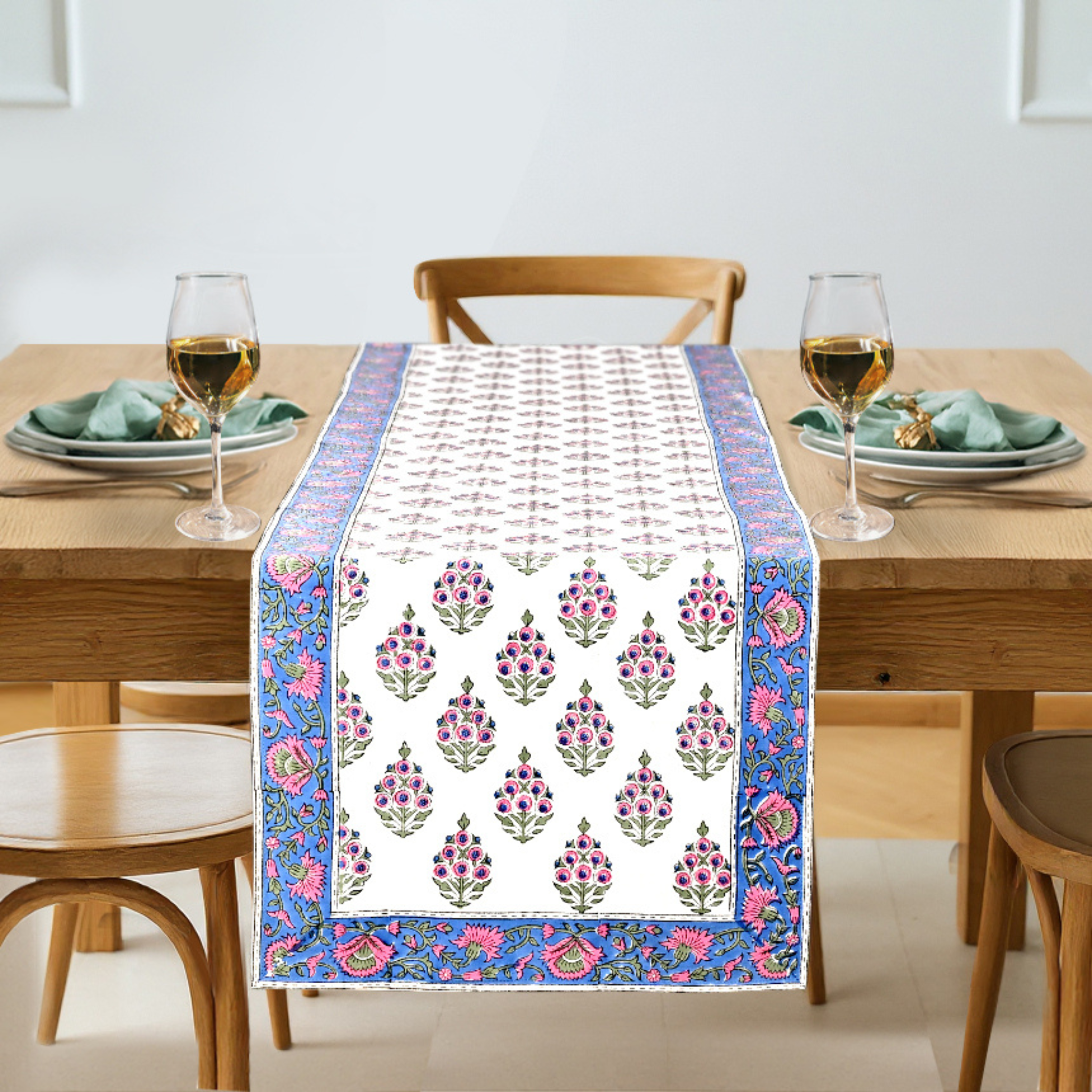 Dining table with a floral patterned table runner, glasses, and plates.