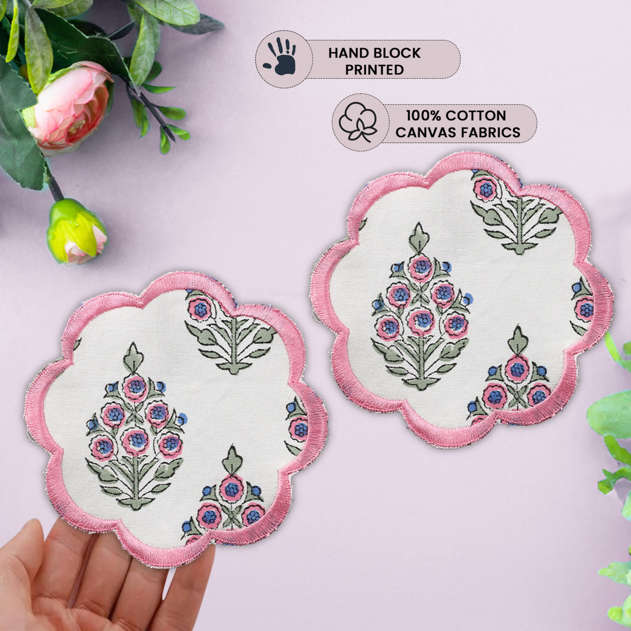 Decorative coasters with floral design held by a hand on a light pink background.