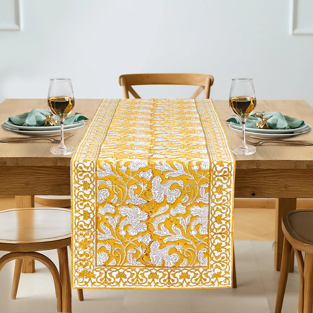 Dining table set with a yellow and white patterned table runner, glasses, plates, and napkins.