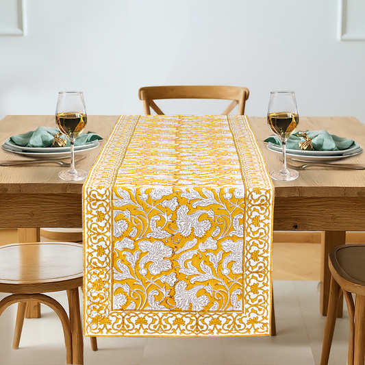 Dining table set with a yellow and white patterned table runner, glasses, plates, and napkins.
