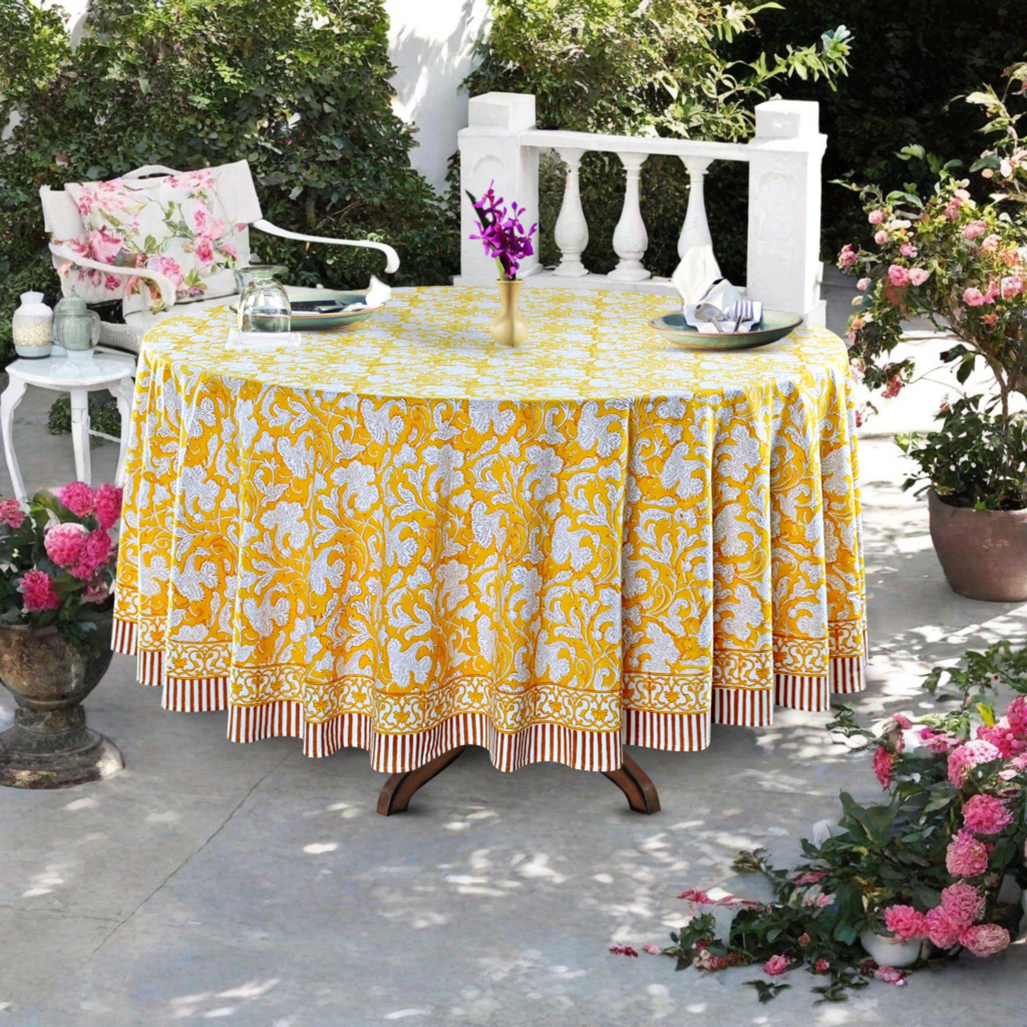 Outdoor table setting with a yellow floral tablecloth, chairs, and decorative elements.