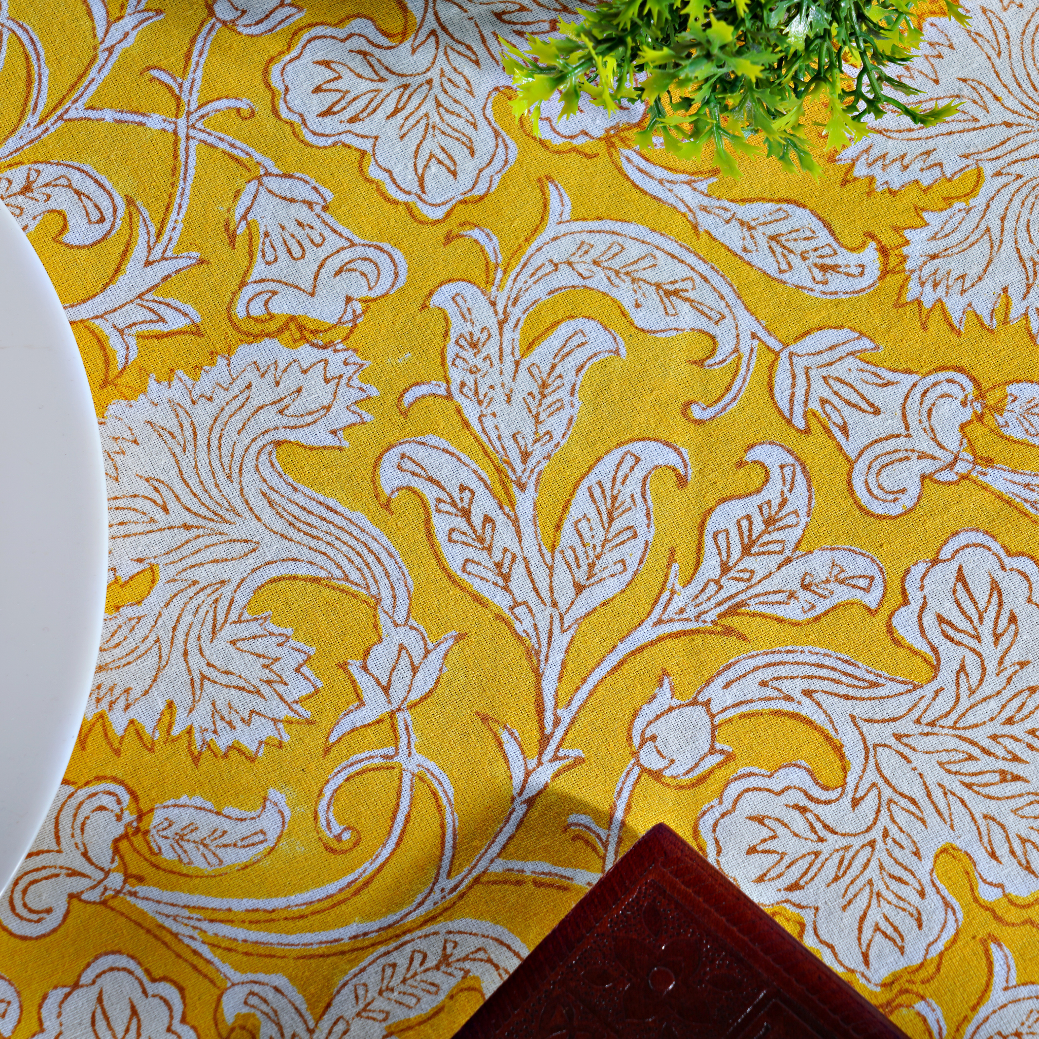 Yellow fabric with white floral pattern, partially covering a plant and a plate.