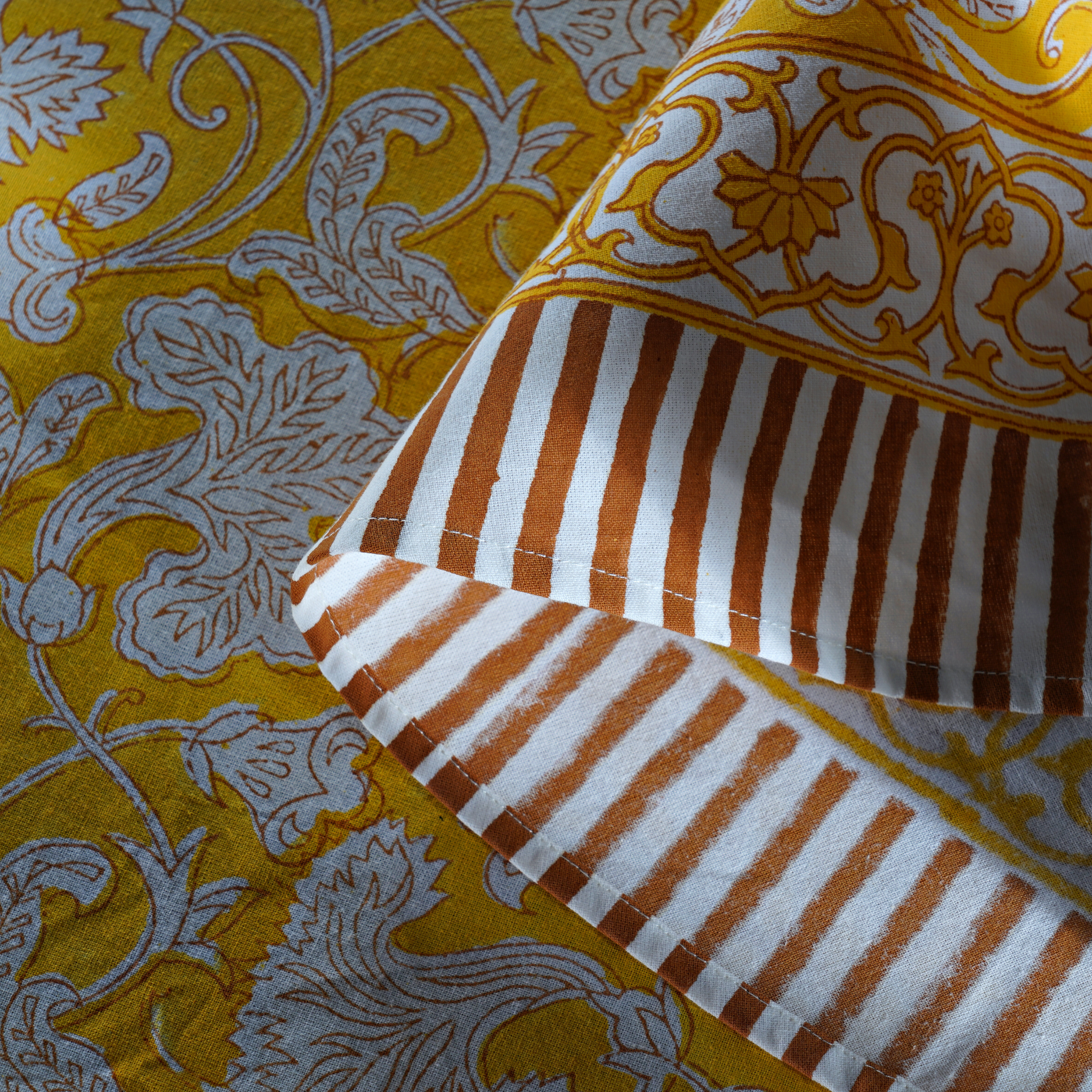 Close-up of a fabric with yellow and white floral pattern and brown and white striped section.