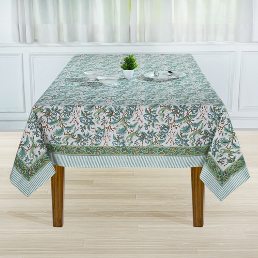 Tablecloth with floral pattern on a wooden table in a room with white curtains.