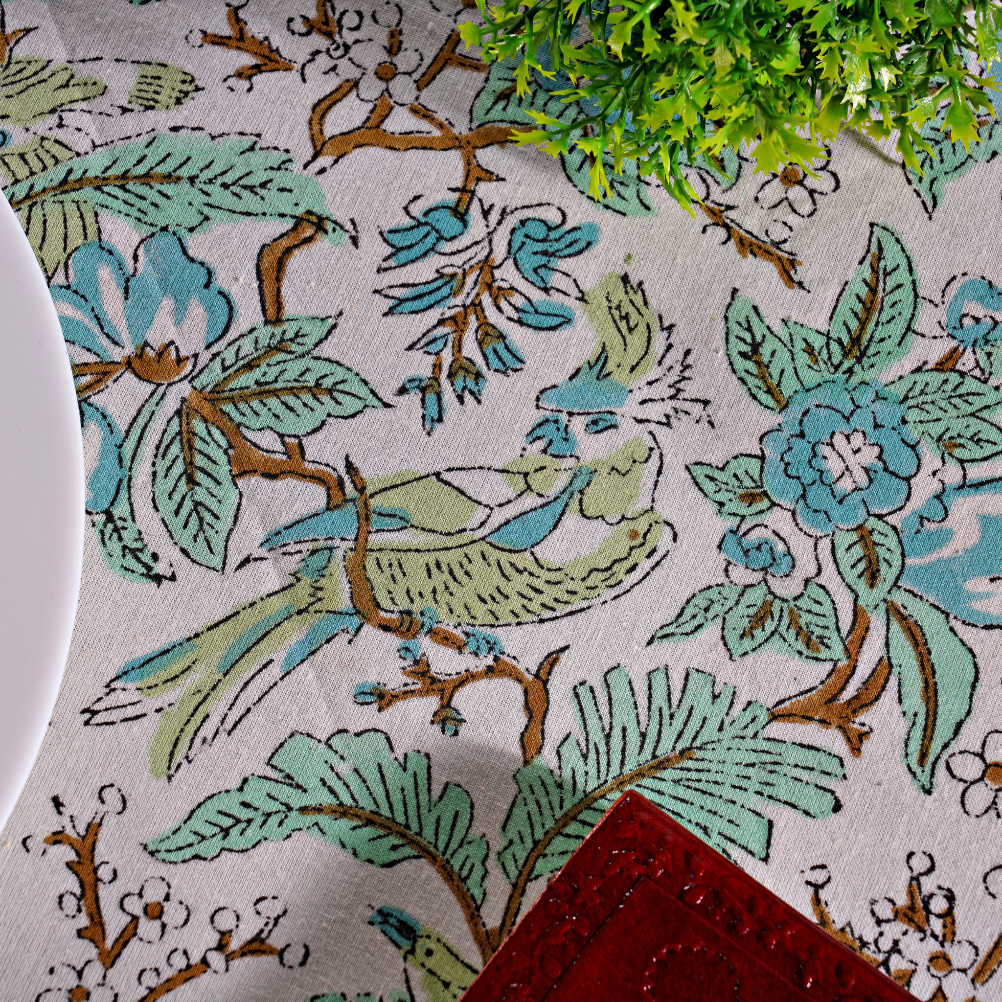 Close-up of a floral and bird patterned fabric with greenery and a red napkin.