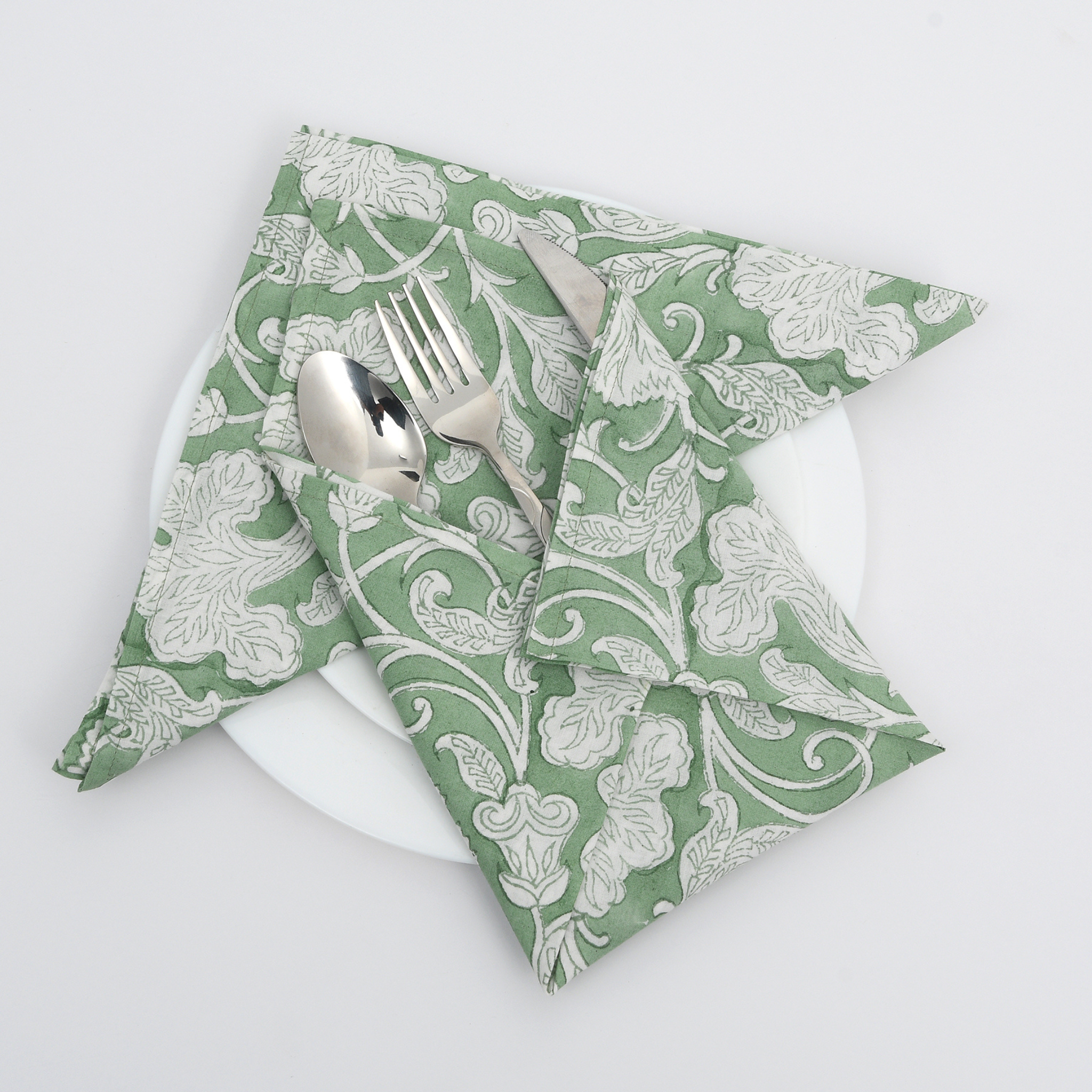 Green floral-patterned napkin with a fork and spoon on a white plate against a light gray background