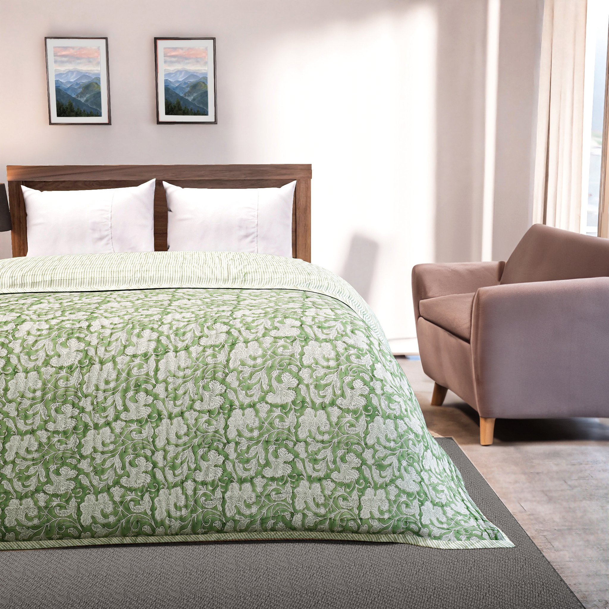 Bedroom with a bed covered in a green floral quilt, a brown armchair, and framed mountain landscapes on the wall.