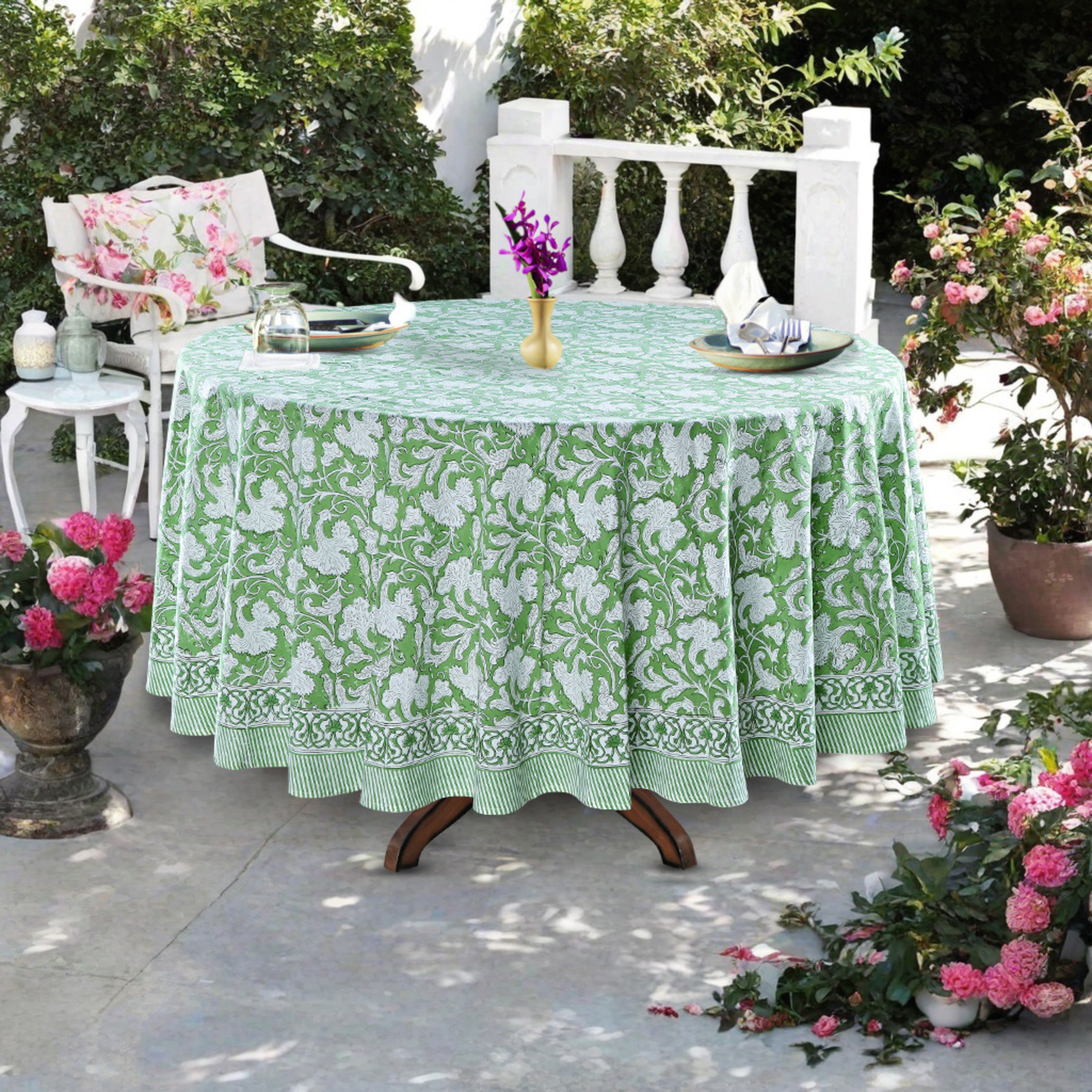 Outdoor table setting with a green floral tablecloth, chairs, and decorative elements.