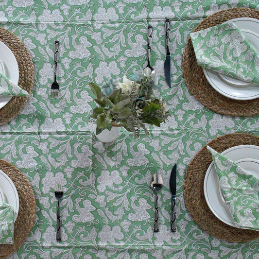 Table setting with green and white patterned tablecloth, plates, napkins, and cutlery.