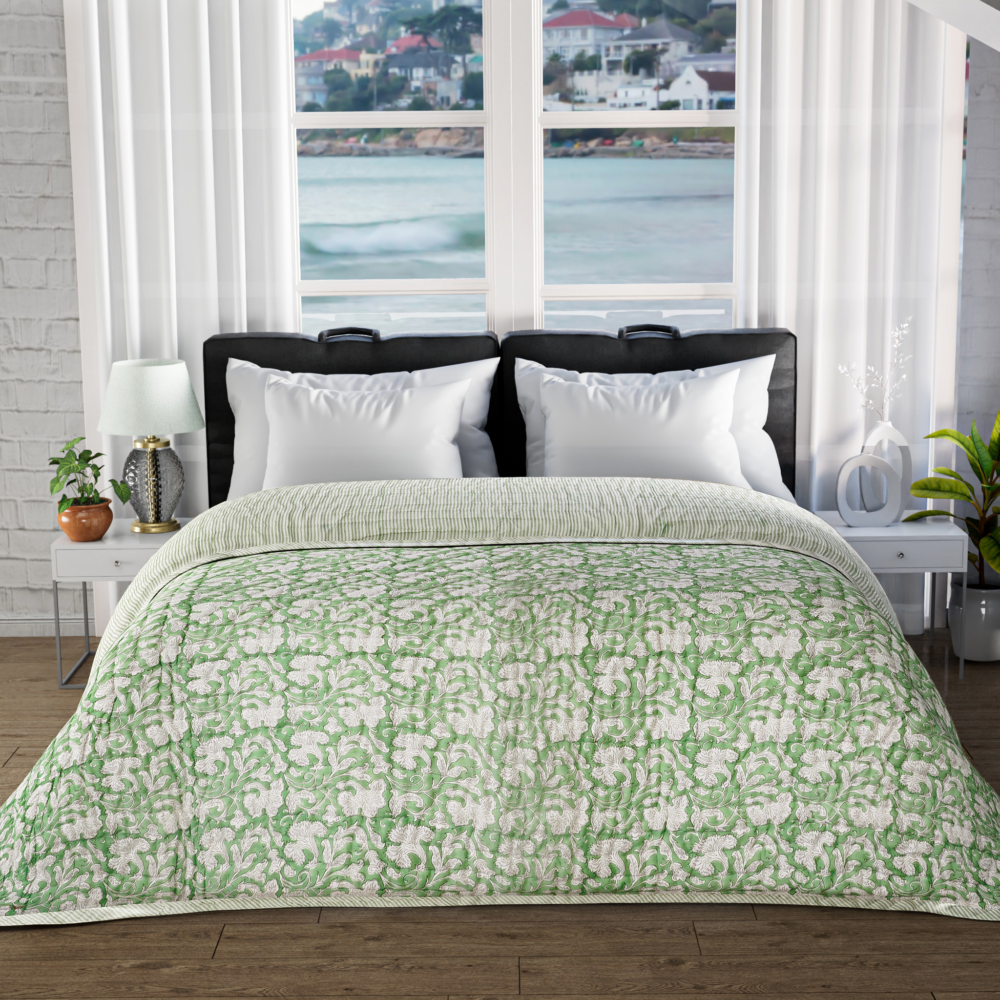 Bed with green floral comforter in a room with large windows showing a view of water and buildings.