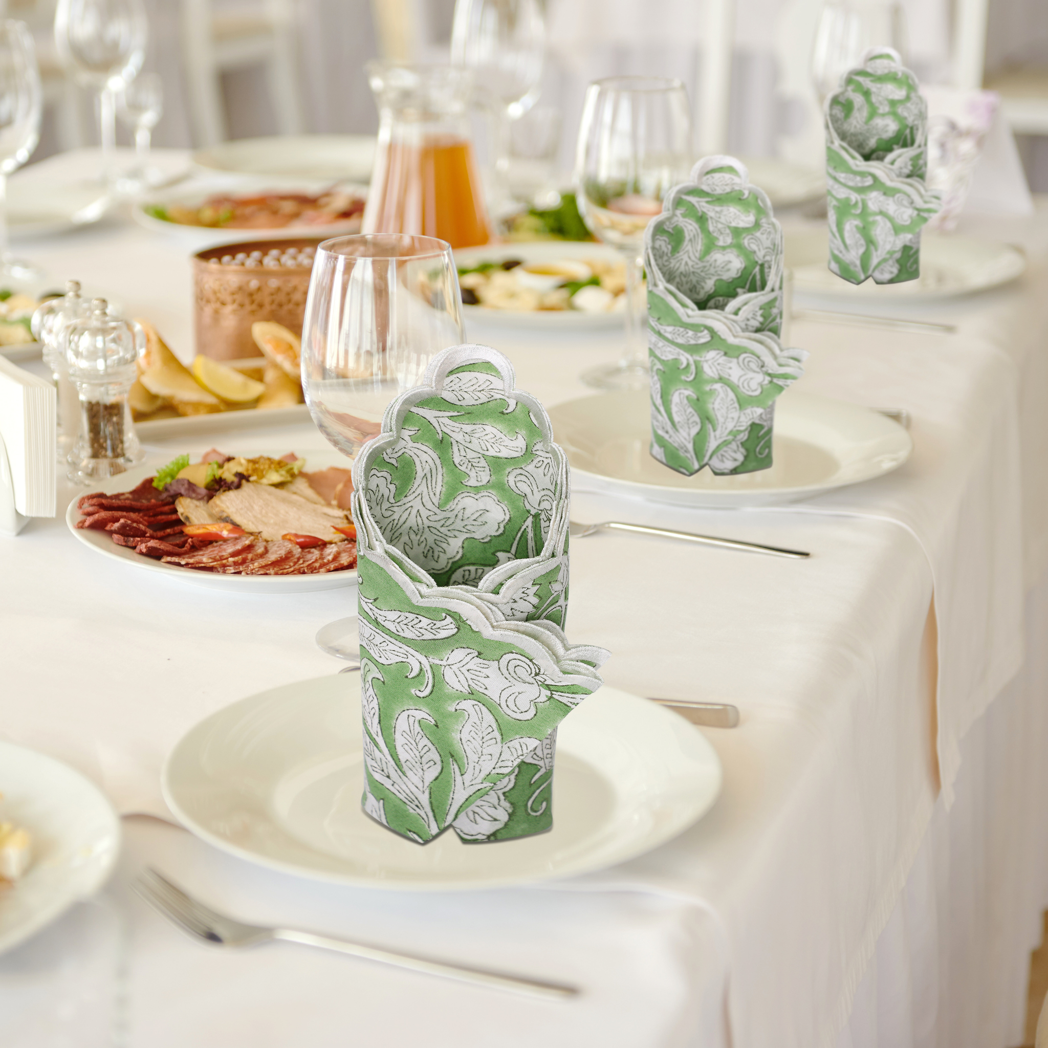 Decorative green and white napkins on a table set with plates and glasses.