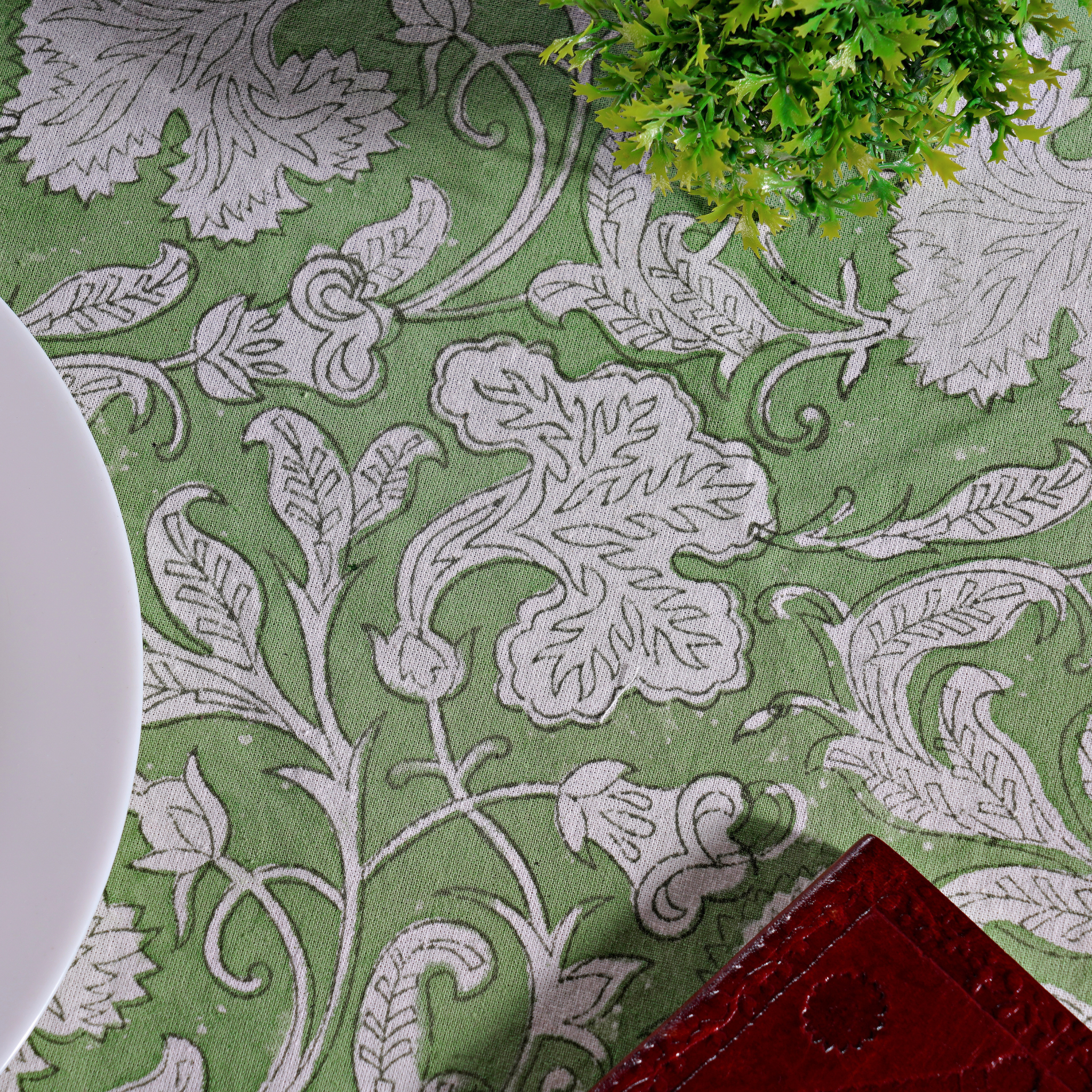 Close-up of a green fabric with white floral patterns, a plant, and a red object.