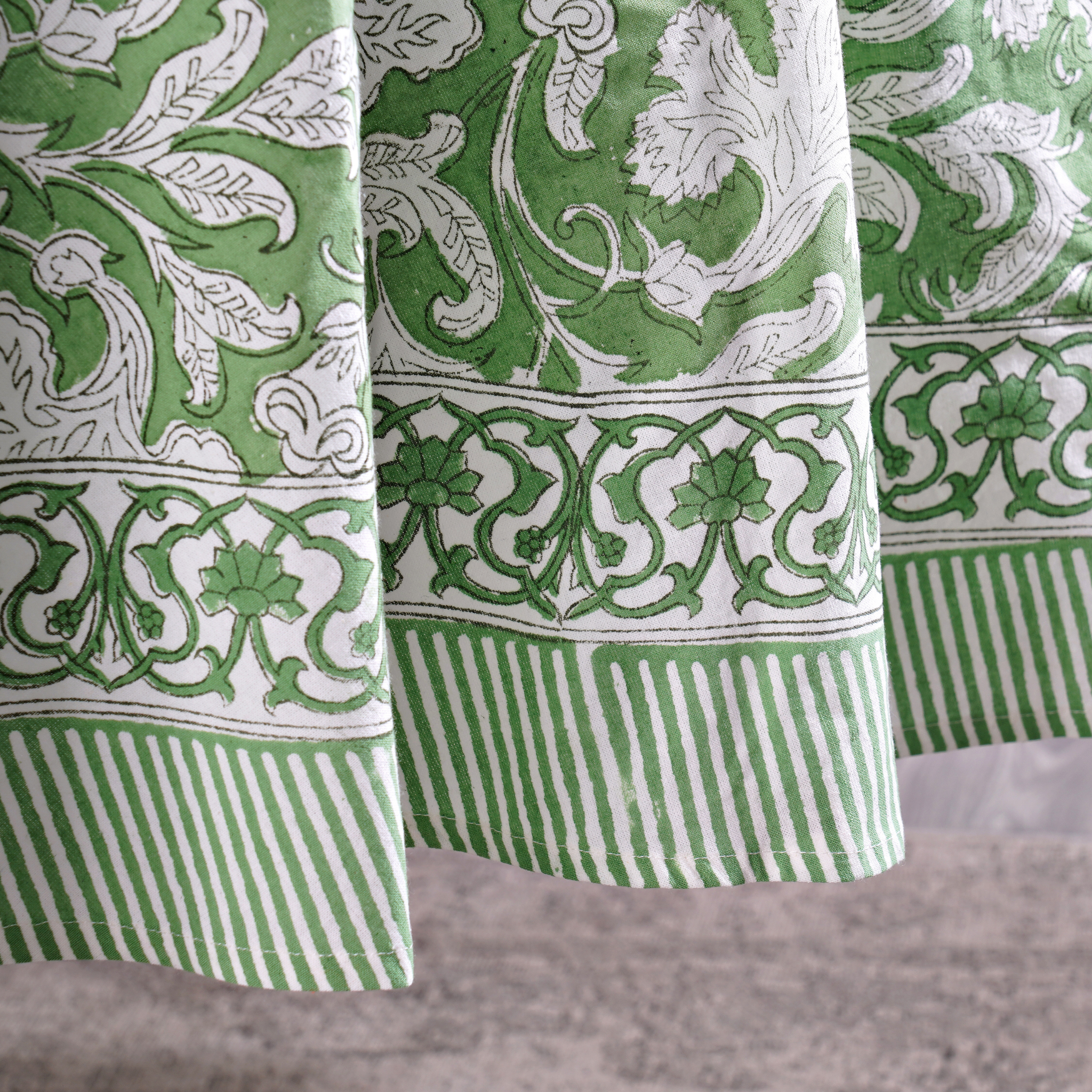 Green and white patterned fabric with floral and striped designs on a gray background