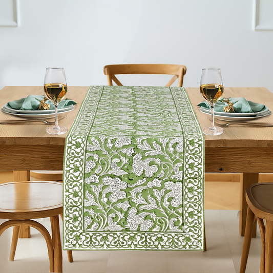 Dining table set with a green and white patterned table runner, glasses, and plates.