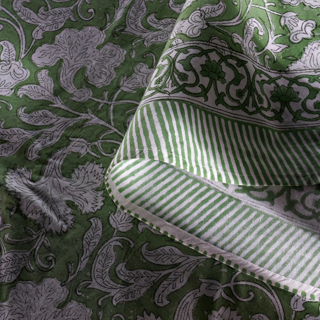 Green fabric with intricate patterns and a folded green and white striped fabric on top