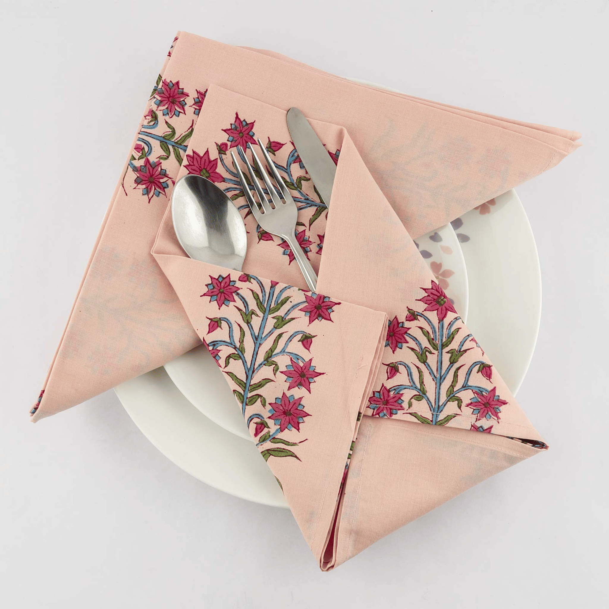 Folded floral-patterned napkin with cutlery on a white plate against a light background