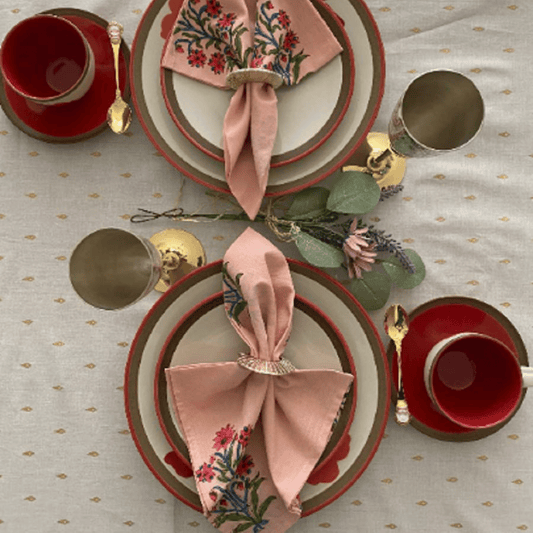 Elegant table setting with red cups, gold saucers, and floral napkins on a patterned tablecloth.