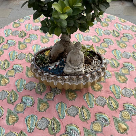 Decorative pot with a Buddha statue and plant on a pink fabric background with leaf pattern