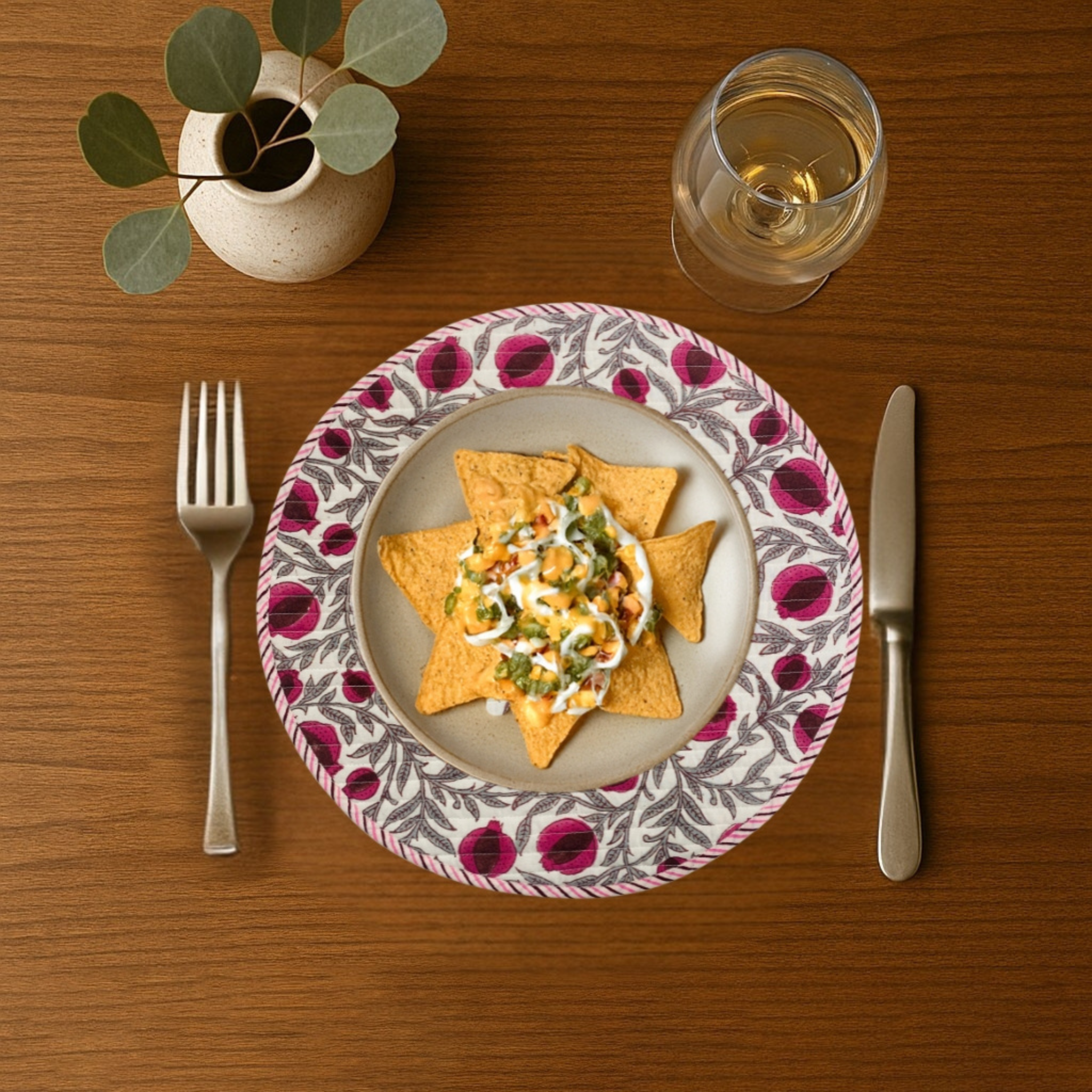 Dinner setting with a plate of nachos, a glass of wine, fork, and knife on a wooden table.