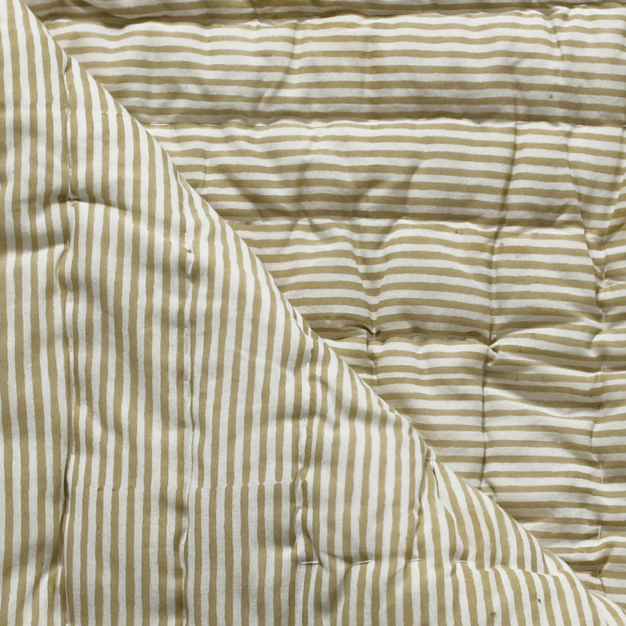 Close-up of a striped quilt with beige and white lines.