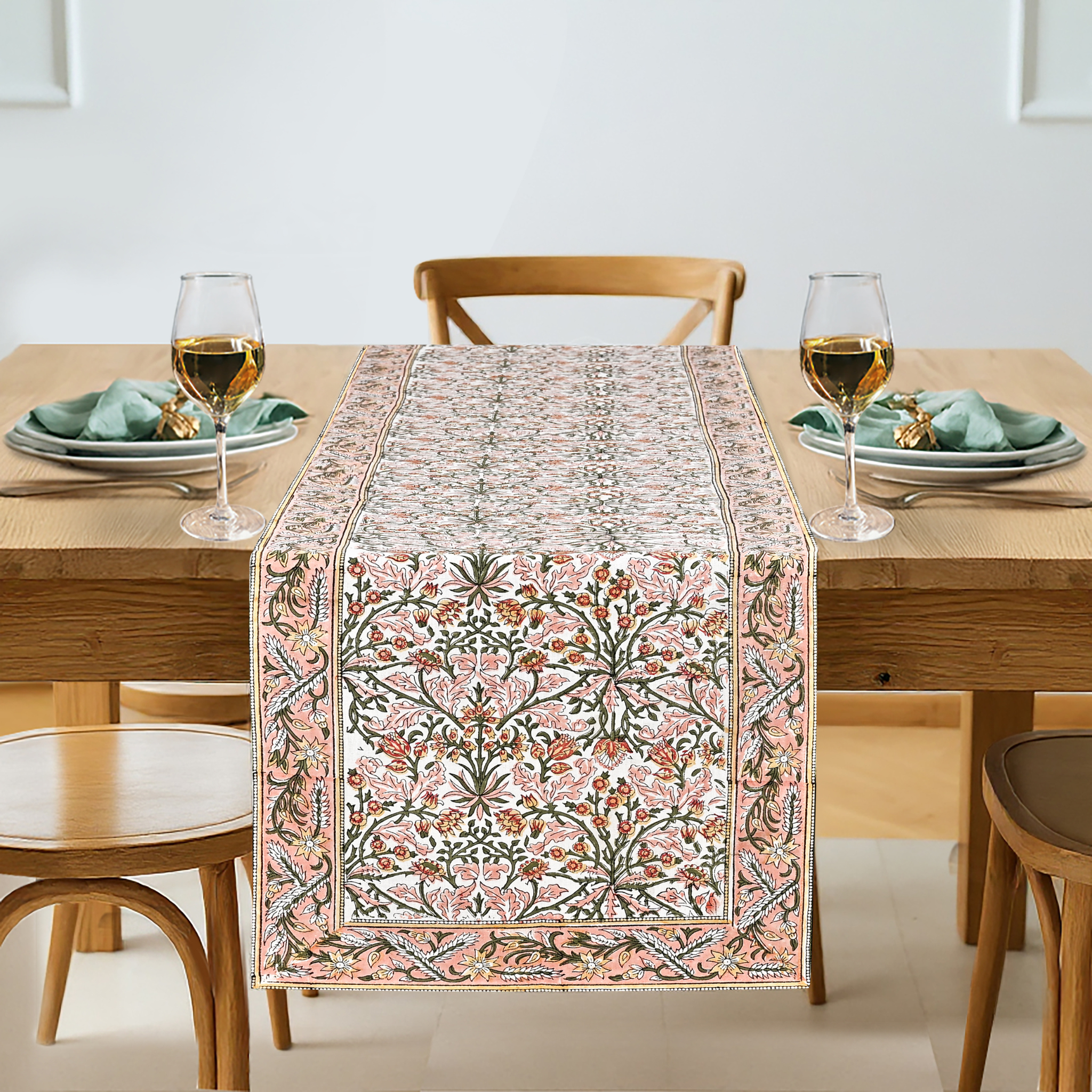 Dining table set with a floral patterned table runner, glasses, and plates.