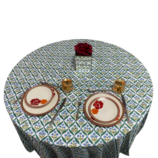 Round table with floral patterned tablecloth, plates, and glasses on a white background