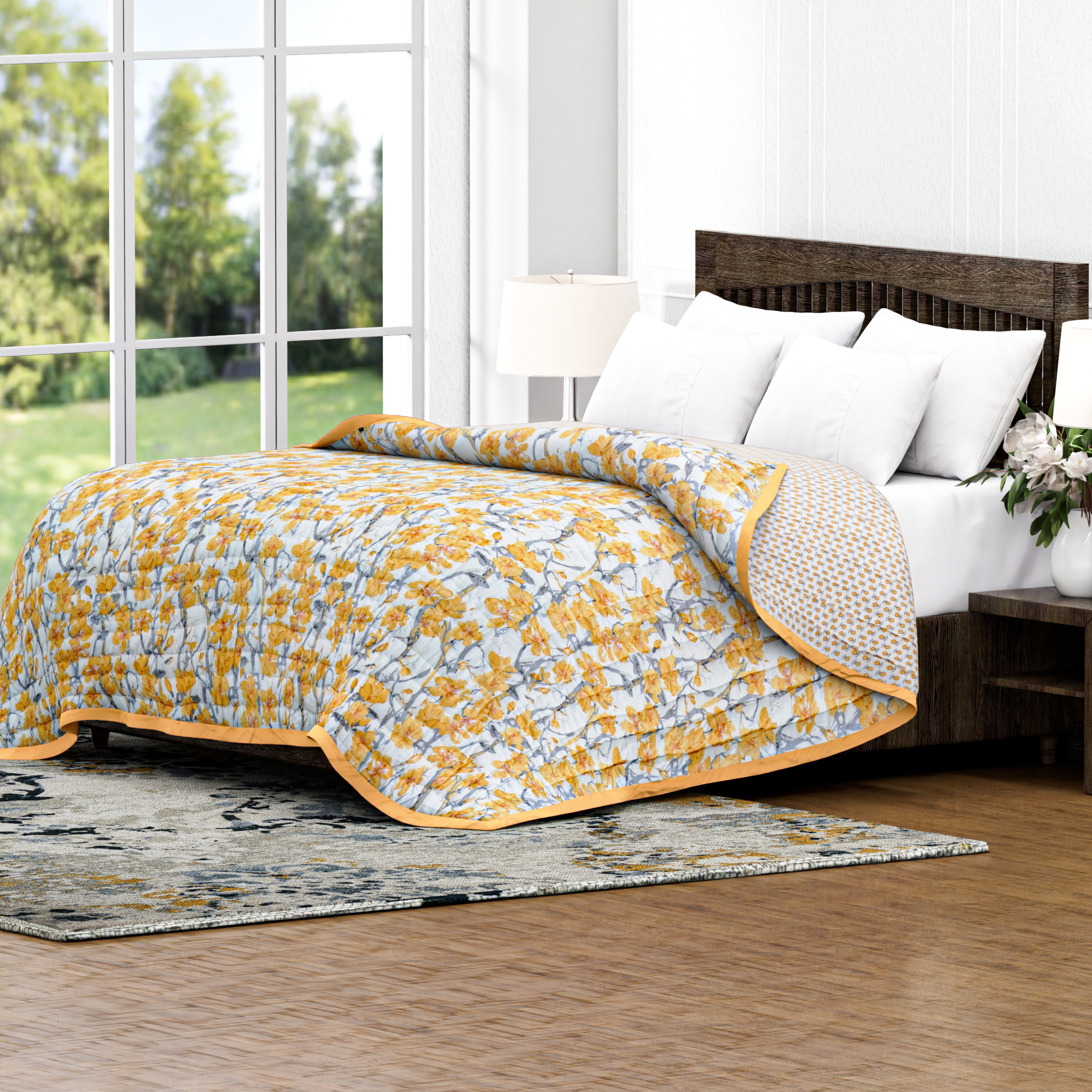 Bed with yellow and white floral quilt in a bright room with large windows.