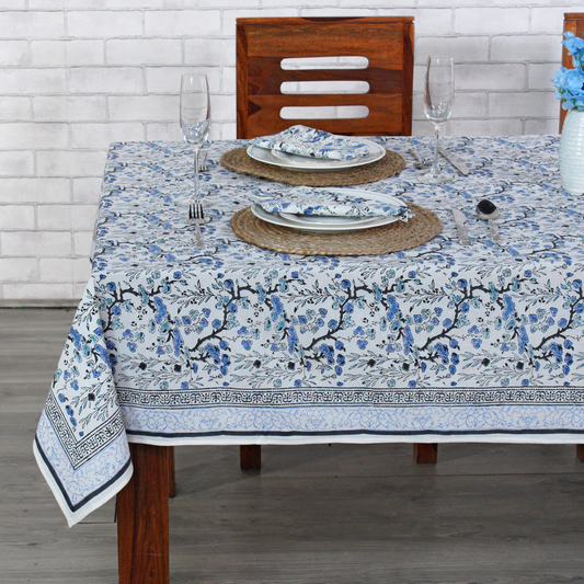 Dining table set with a floral tablecloth, plates, and glasses on a wooden table.