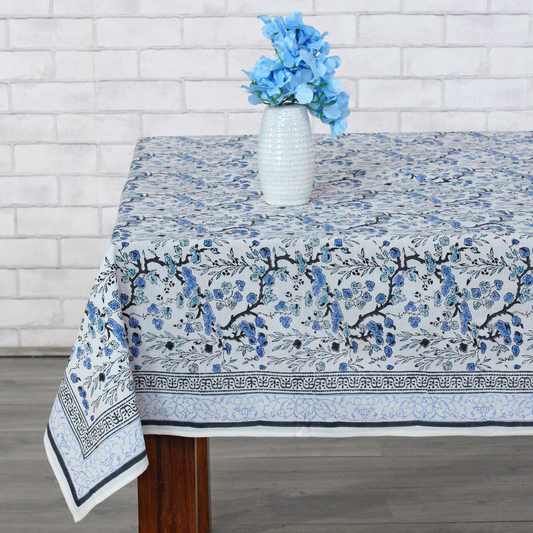 Tablecloth with floral design on a wooden table against a white brick wall.