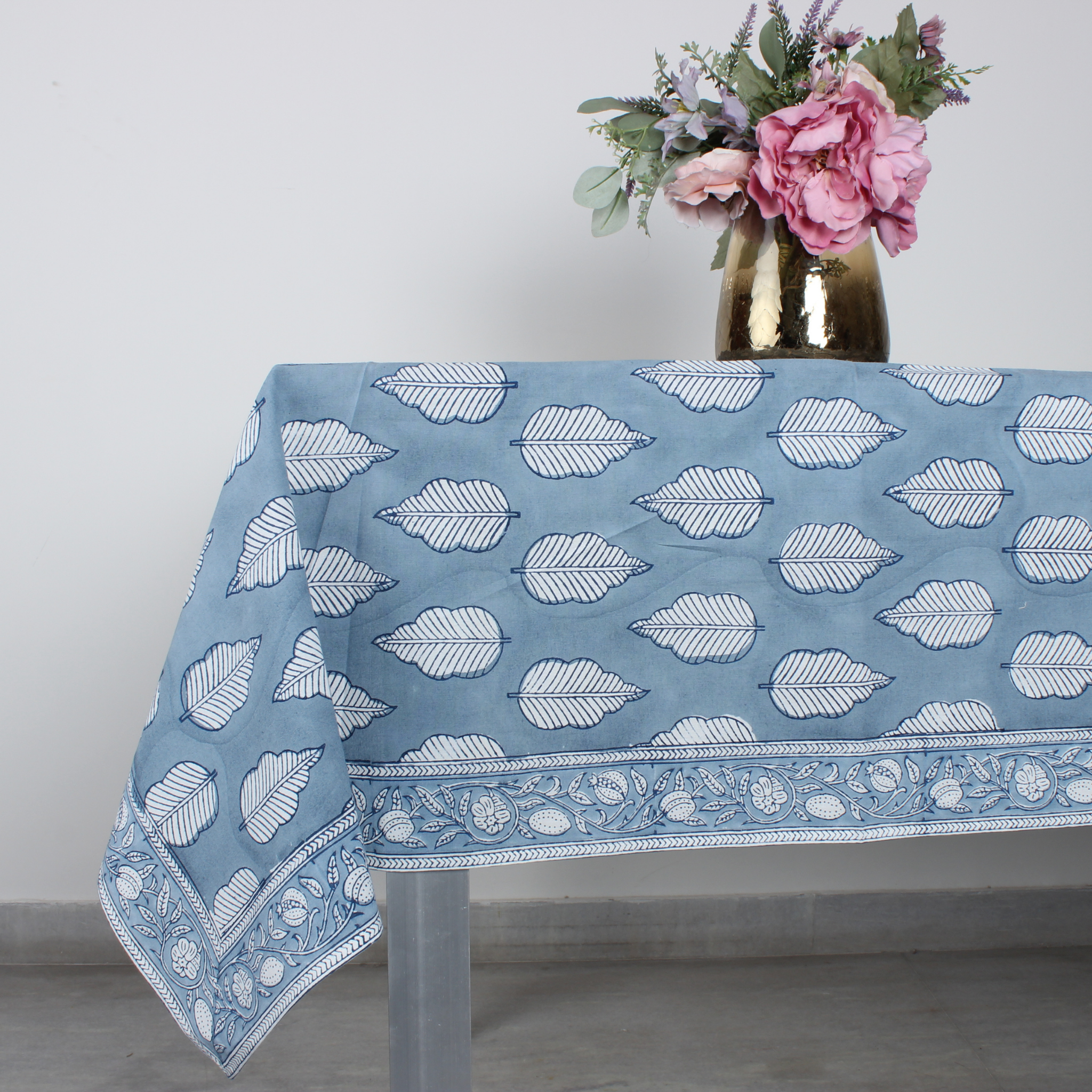 Blue tablecloth with white leaf pattern on a table with a vase of flowers.