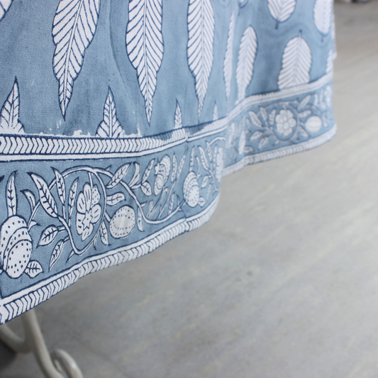 Close-up of a blue tablecloth with white floral patterns on a wooden surface.