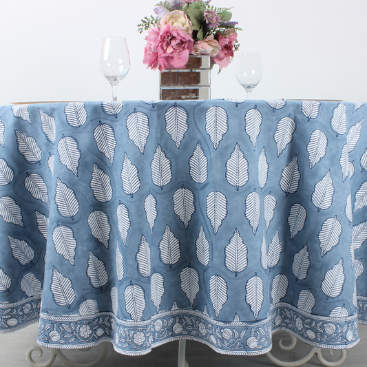 Blue tablecloth with white leaf pattern on a table with flowers and glasses.