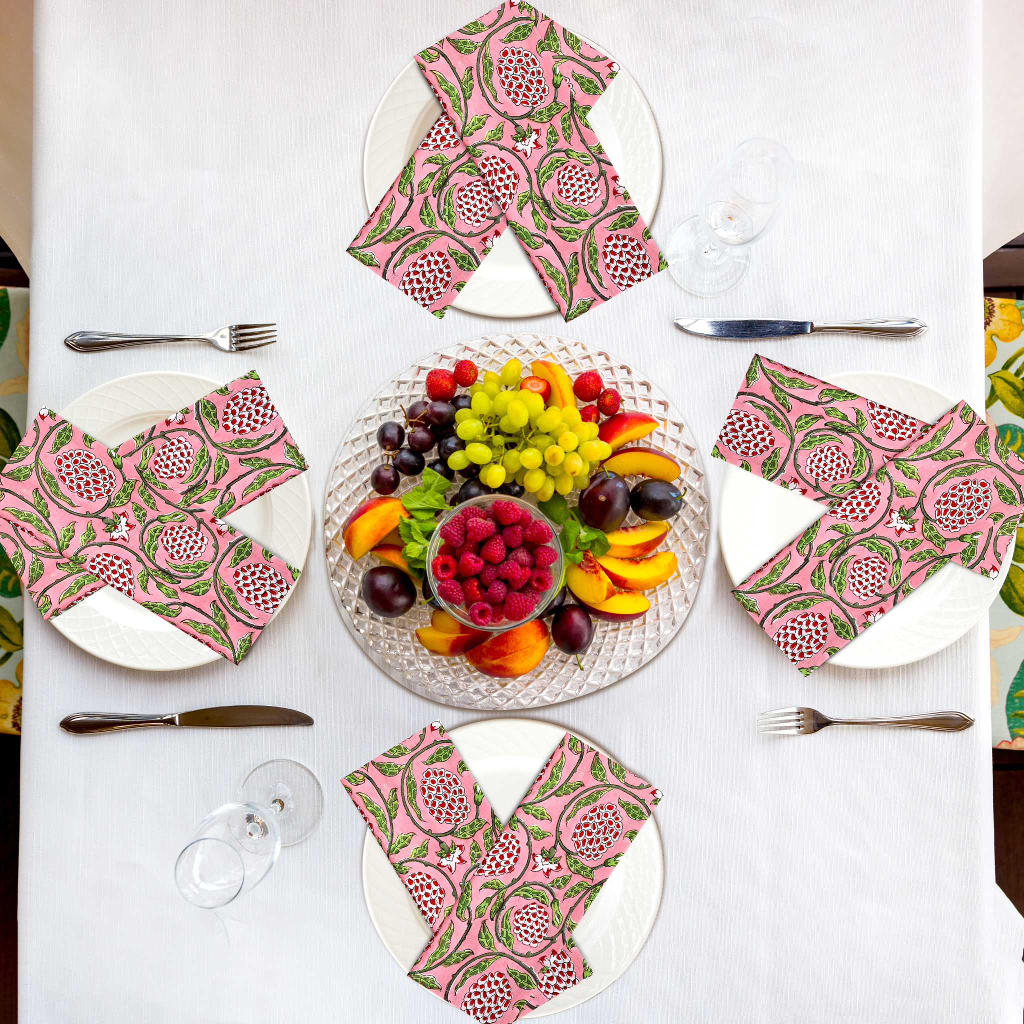 Table setting with fruit platter and floral napkins on a white tablecloth.