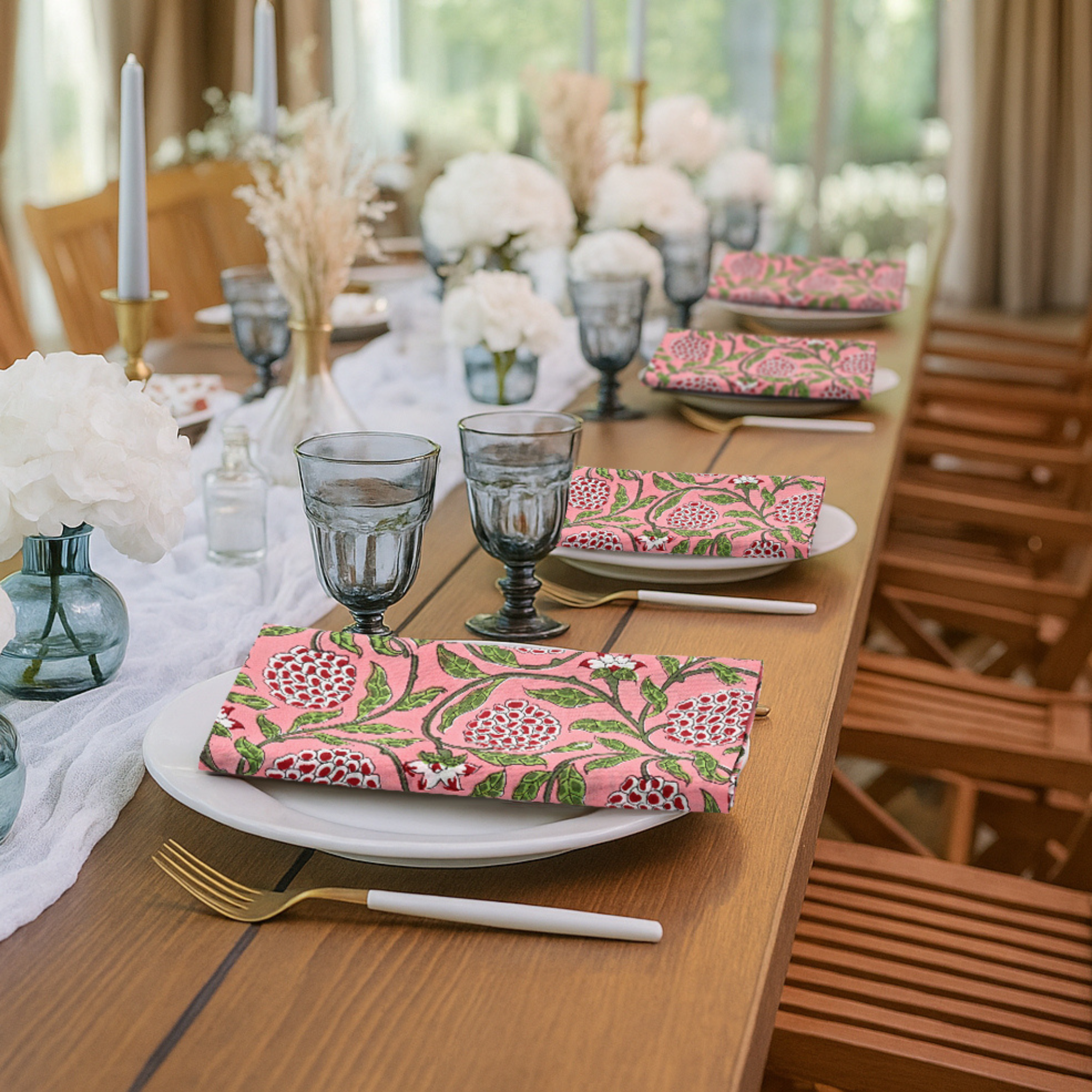 Dining table set with floral-patterned plates, glasses, and napkins in a bright room.