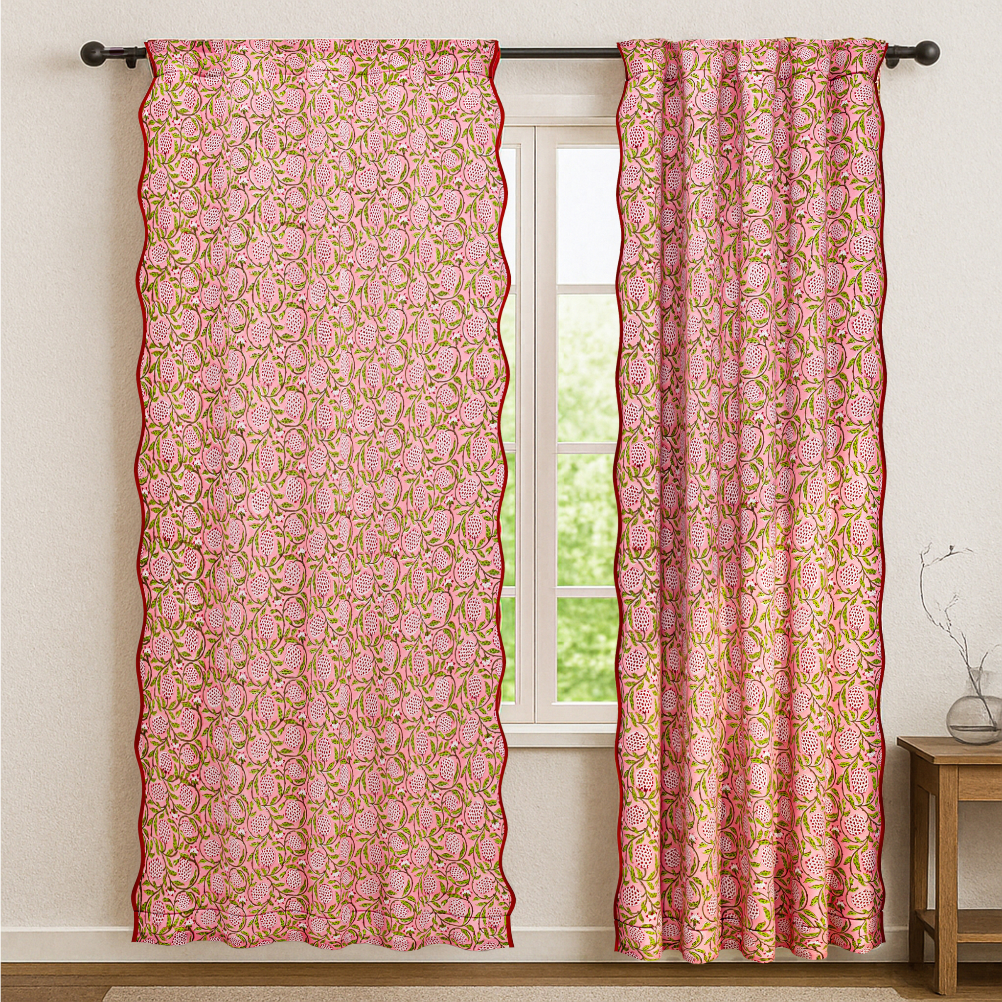 Pink floral patterned curtains hanging in front of a window with a white wall and wooden side table in the background.