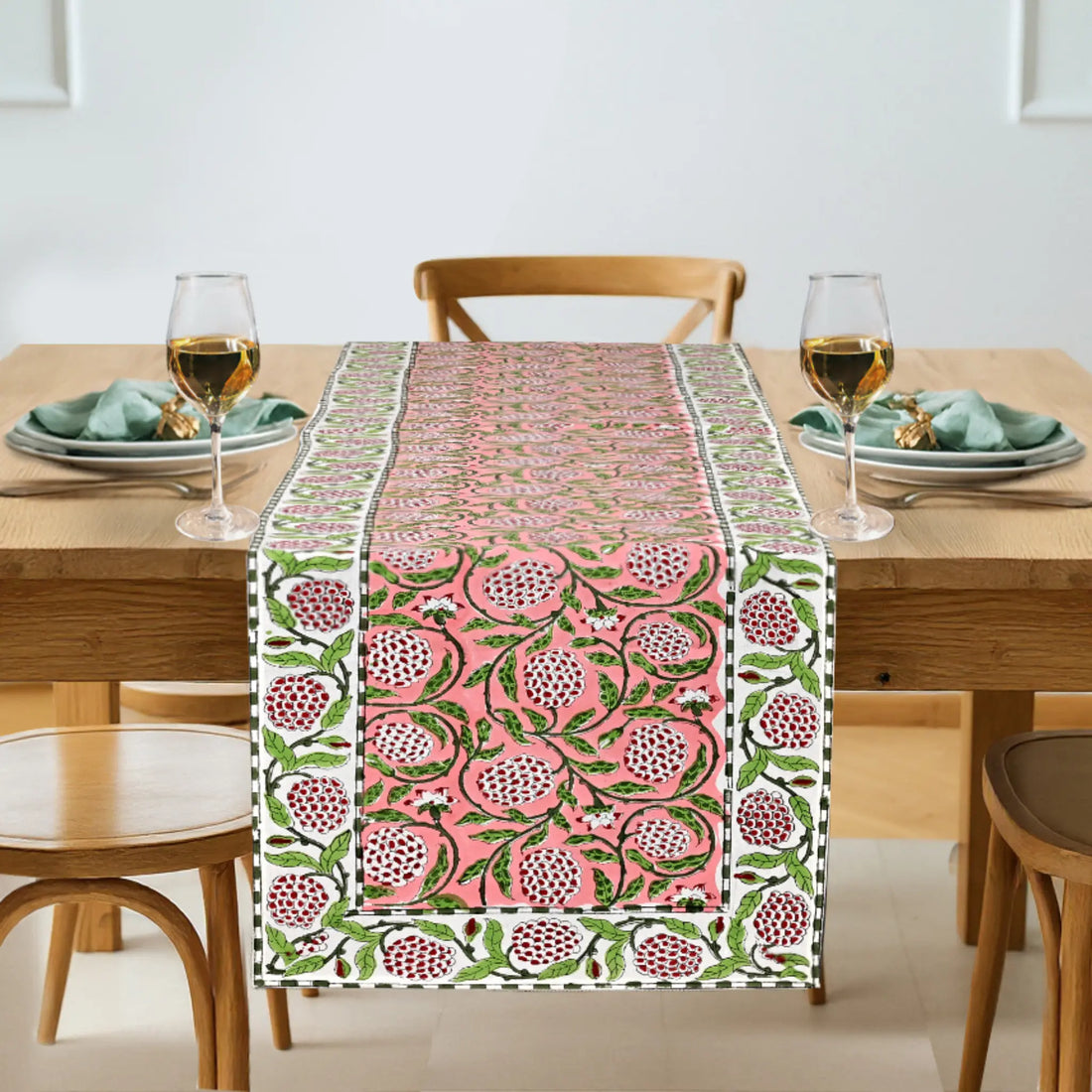 Table setting with a pink and green patterned table runner on a wooden table.