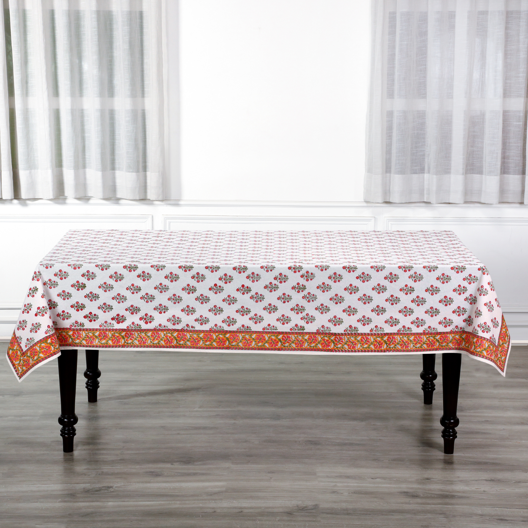 Tablecloth with a floral pattern on a wooden table in a room with white curtains.