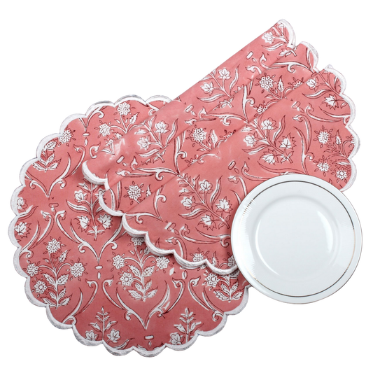 Set of pink floral-patterned placemats with a white plate on a white background
