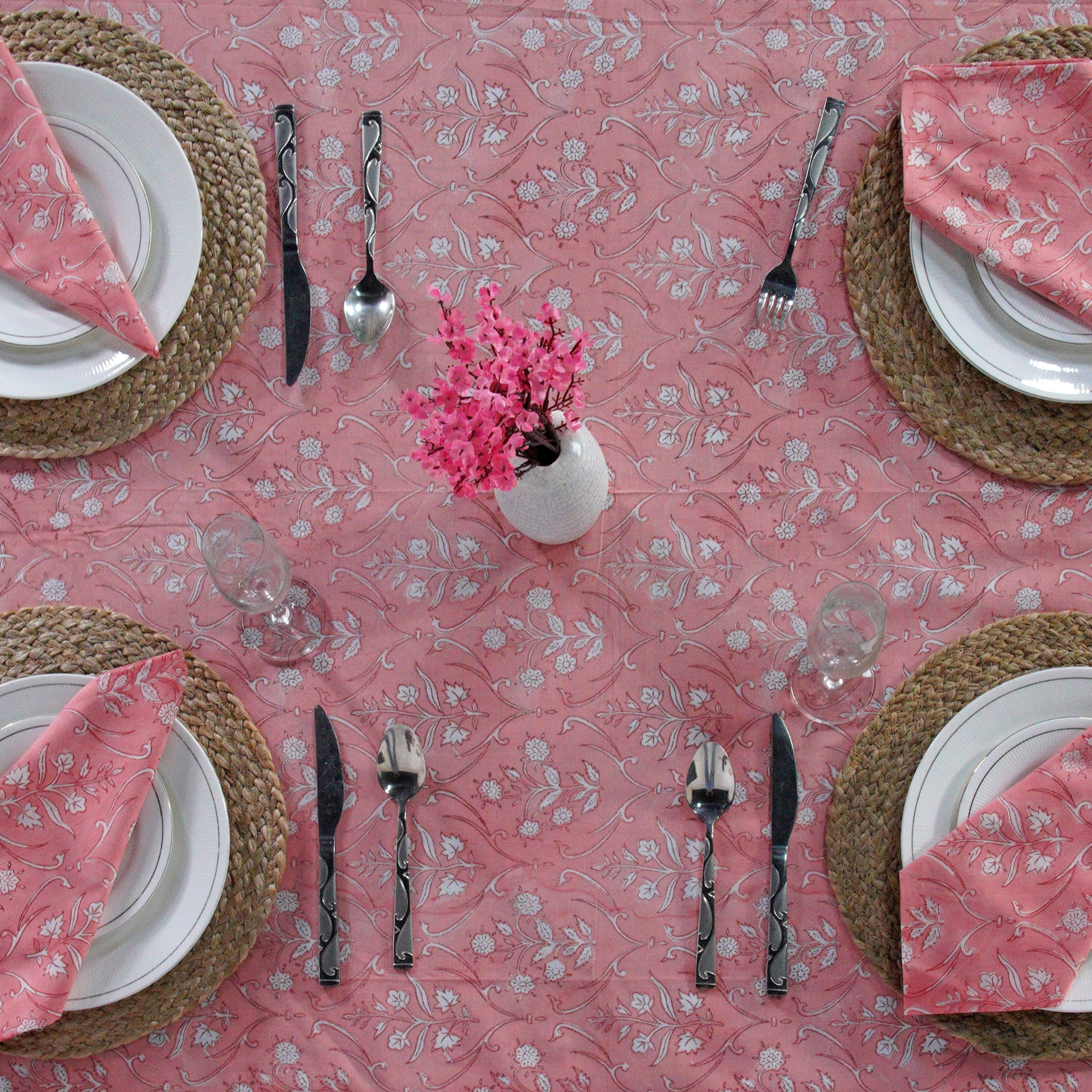 Dining table setting with pink floral tablecloth, plates, cutlery, and napkins.