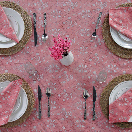 Dining table setting with pink floral tablecloth, plates, cutlery, and napkins.